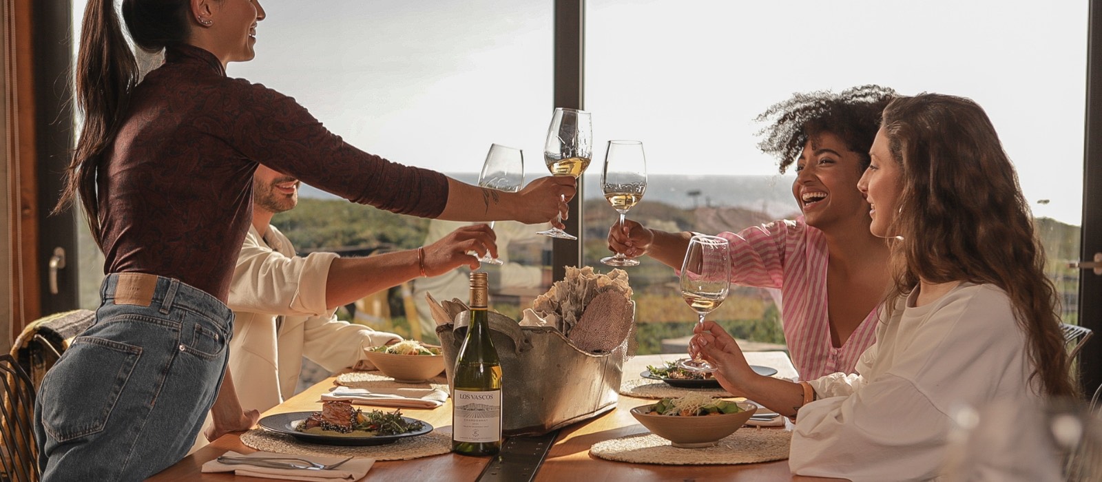 Mesa elegante de fim de tarde com taças de vinho, garrafa gelada e clima de happy hour ao ar livre